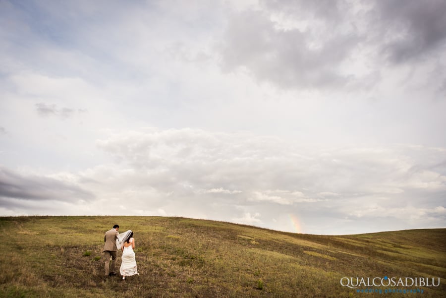 bride and groom walking open field rainbow