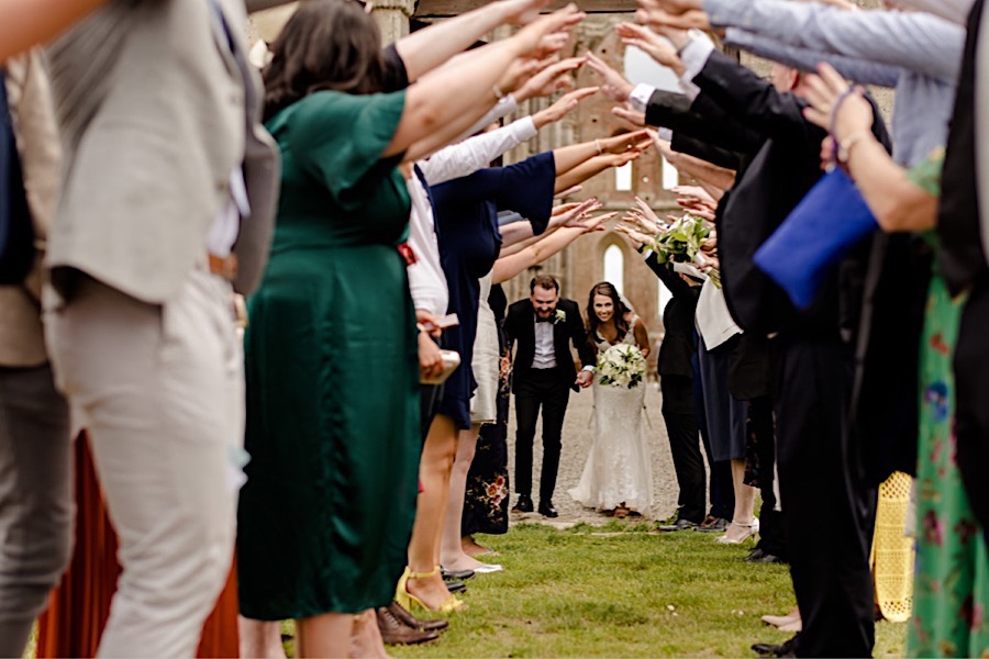 bride and groom passing down the tunnel created with arms of the guests