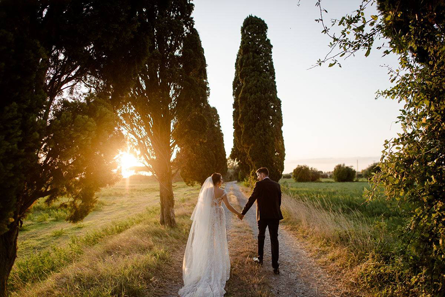 a wedding couple walking in tuscany during the golden hour in a cypresses road