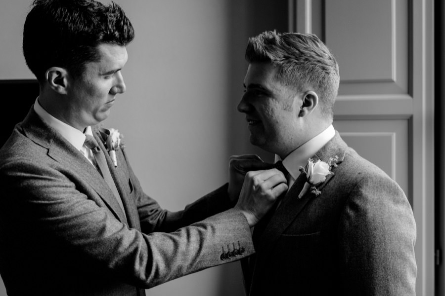 groom is helping his groomsman during the getting ready black and white photo