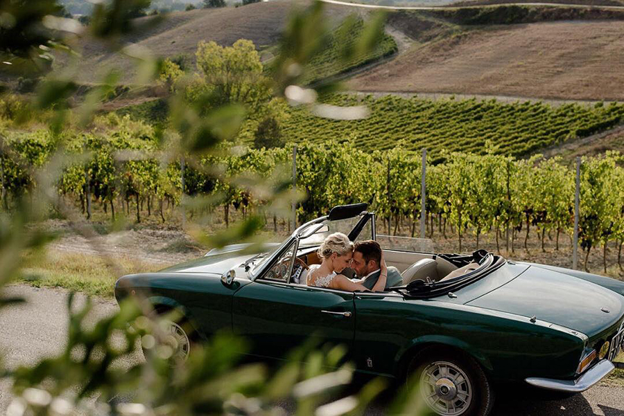 wedding couple embraced in a car immersed in the middle of the tuscany countryside