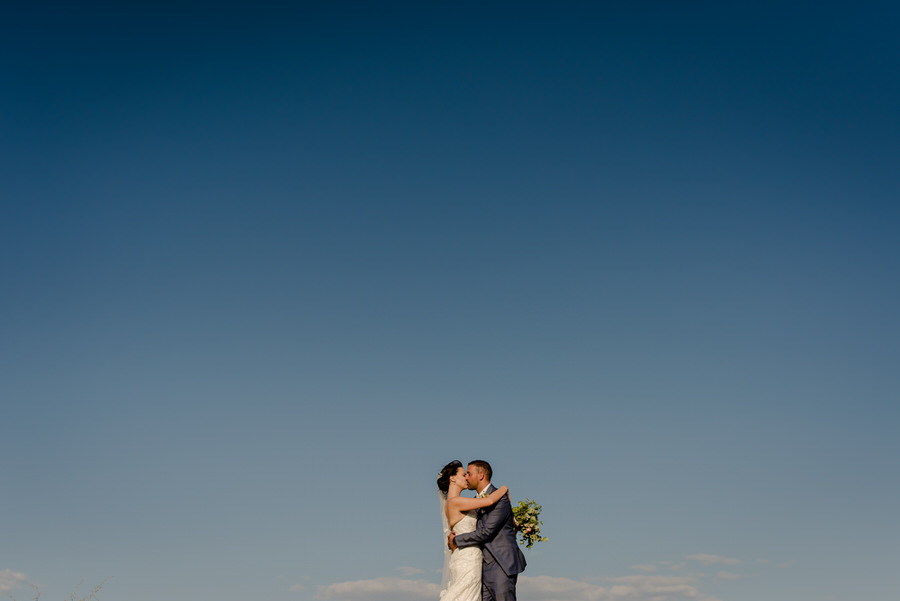 Bride and groom kissing with the sky in the background