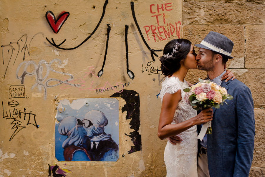 bride and groom are kissing in florence with a painted wall behind